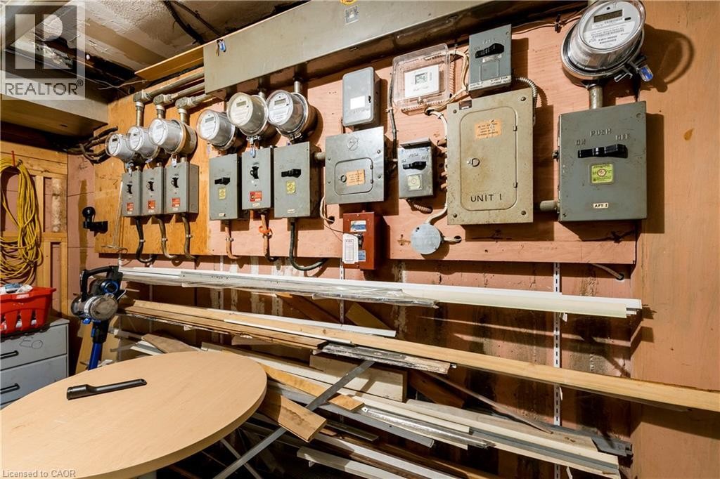 Electrical panels and meters mounted on a wood-paneled wall, featuring exposed conduit and wiring - 43 Sixth Avenue, Kitchener, ON - Indoor