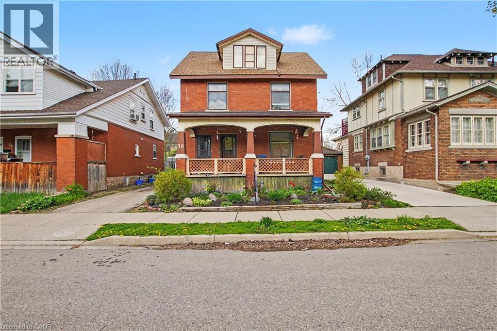 Red brick facade residence featuring a covered front porch with decorative railing, dormer window, and a planted front garden bed - 30 Hohner Avenue, Kitchener, ON - Outdoor