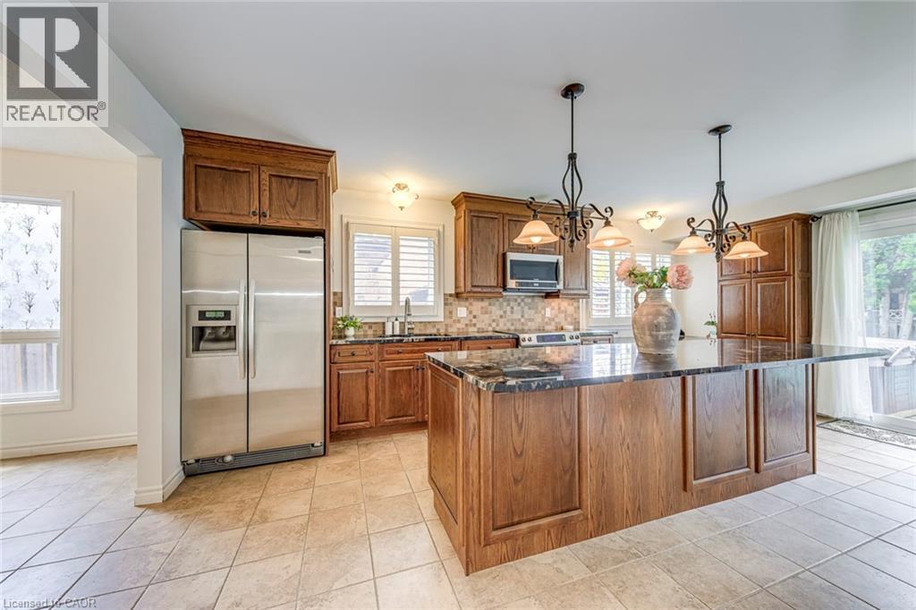 Kitchen featuring a large central island with a dark countertop, wood-finish cabinetry, stainless steel appliances, tile flooring, and two chandelier-style pendant lights - 43 Niska Drive, Waterdown, ON - Indoor Photo Showing Kitchen