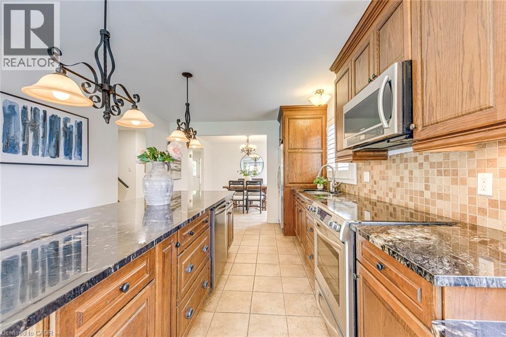Kitchen featuring wood cabinetry, dark countertops, stainless steel appliances, tile flooring, and a mosaic tile backsplash - 43 Niska Drive, Waterdown, ON - Indoor Photo Showing Kitchen