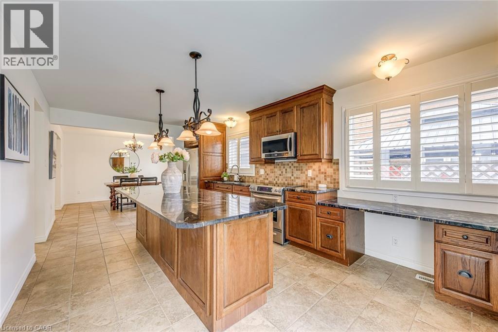 Spacious kitchen featuring an expansive center island with dark countertops, wood cabinetry, stainless steel appliances, and a mosaic tile backsplash - 43 Niska Drive, Waterdown, ON - Indoor Photo Showing Kitchen