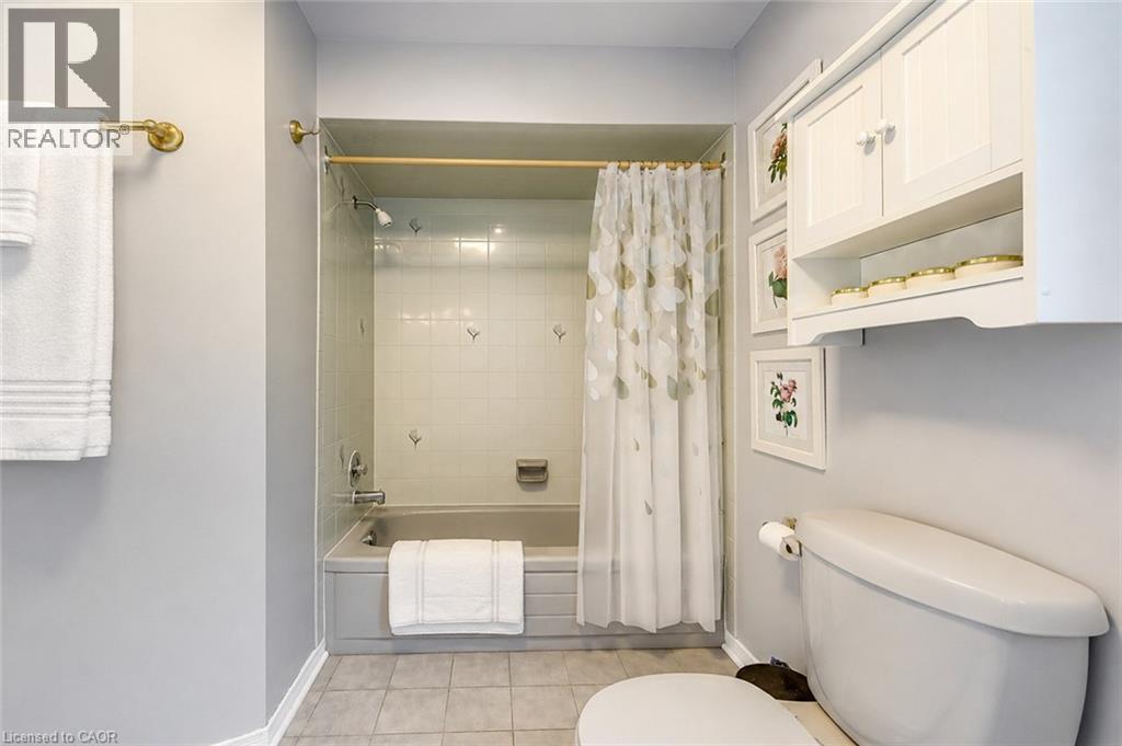 Bathroom featuring a built-in bathtub with subway tile surround, neutral-toned floor tile, and a wall-mounted storage cabinet - 43 Niska Drive, Waterdown, ON - Indoor Photo Showing Bathroom