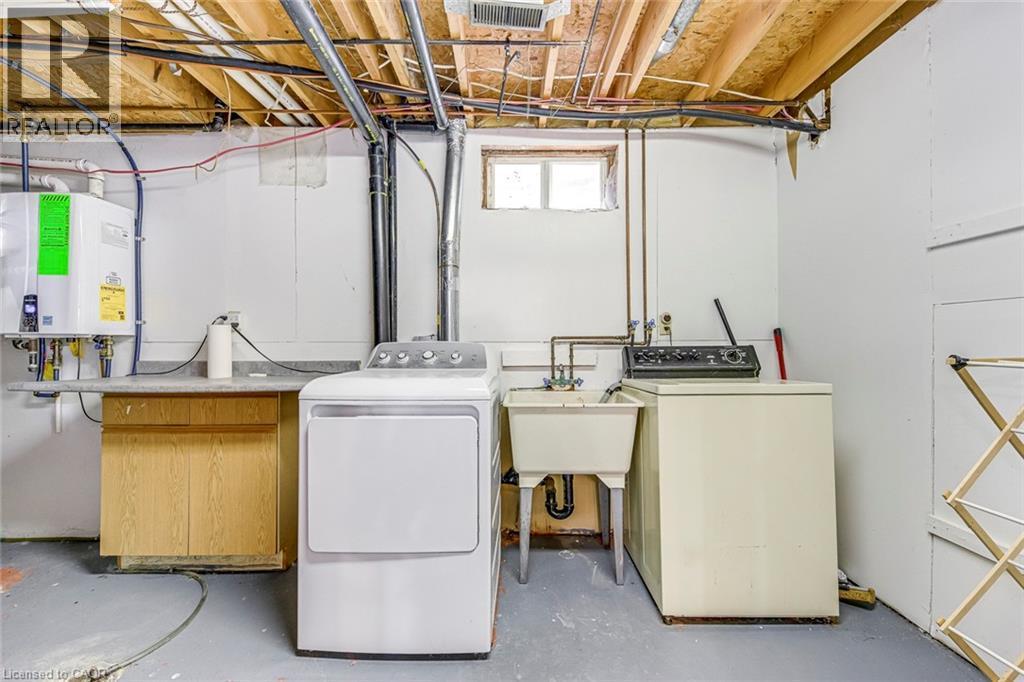 Utility space featuring a service sink, a wood-finish cabinet with a countertop, exposed ceiling joists, and a window providing natural light - 43 Niska Drive, Waterdown, ON - Indoor Photo Showing Laundry Room