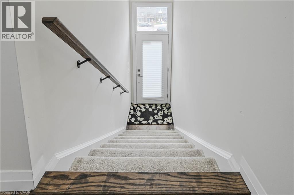 Carpeted staircase featuring a wood-finish handrail with dark metal brackets - 720 Grey Street Unit# 34, Brantford, ON - Indoor Photo Showing Other Room