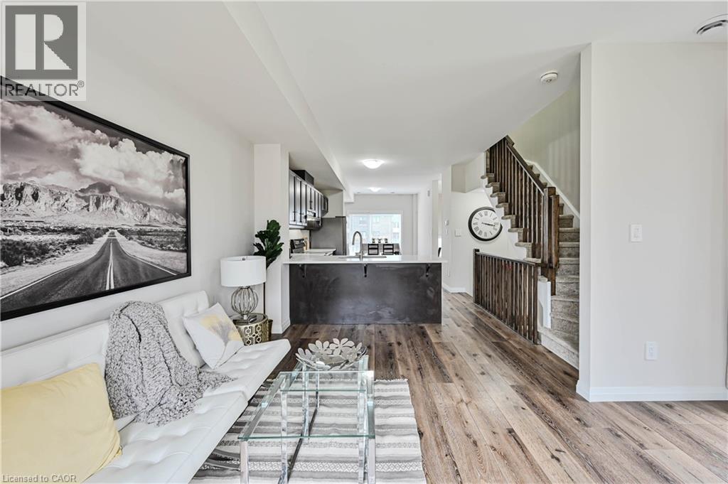 Open-concept living space featuring wood-finish flooring, a kitchen island with a light-toned countertop, dark cabinetry, and a staircase with wood railings - 720 Grey Street Unit# 34, Brantford, ON - Indoor Photo Showing Living Room