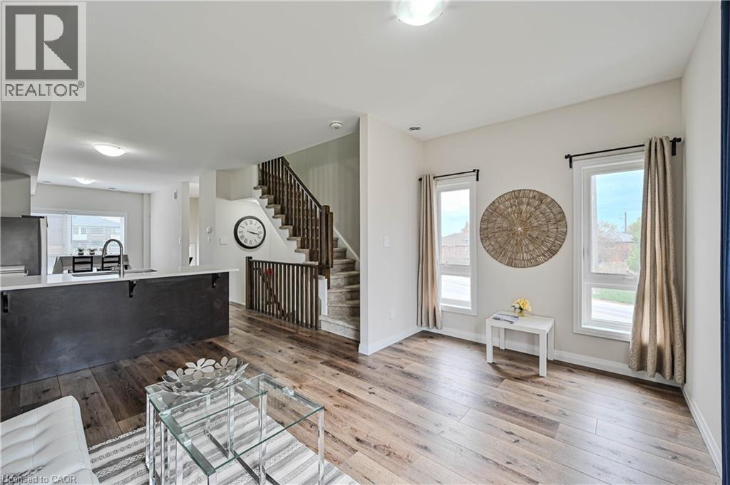 Open-concept living area with wood-finish flooring, white walls, and a staircase featuring dark wood railings - 720 Grey Street Unit# 34, Brantford, ON - Indoor
