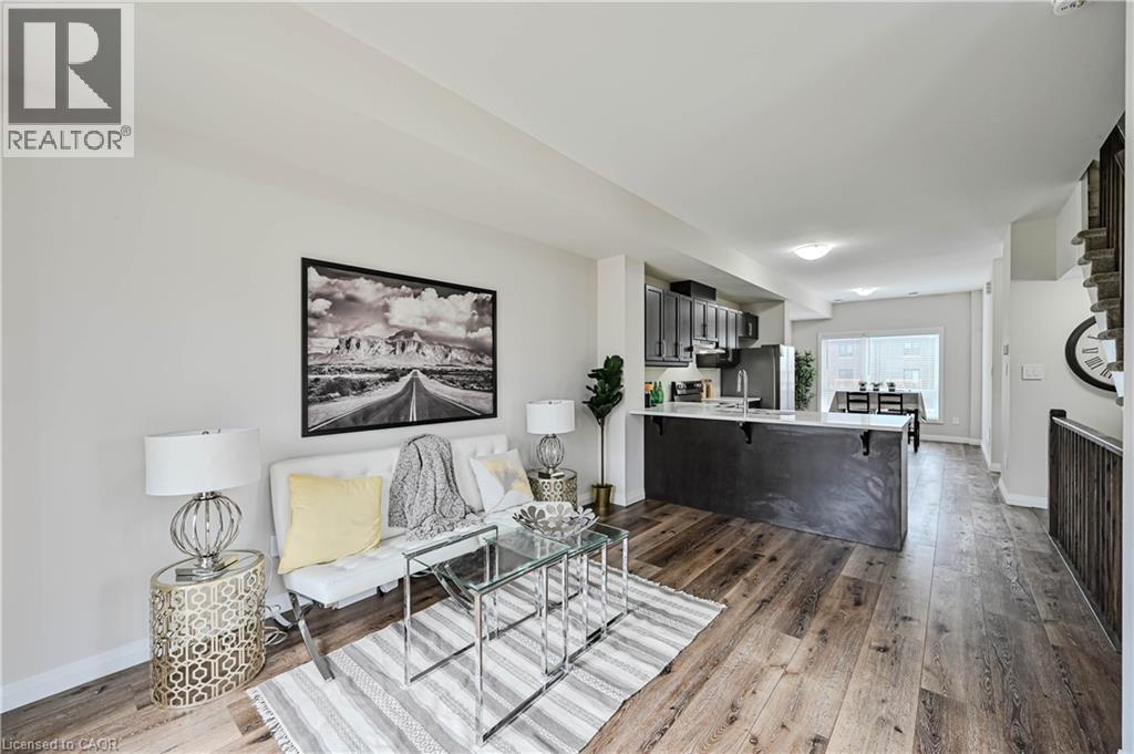 Open-concept living area featuring wood-finish flooring, a contemporary kitchen island with a light-toned countertop, dark cabinetry, and integrated stainless steel appliances - 720 Grey Street Unit# 34, Brantford, ON - Indoor Photo Showing Other Room