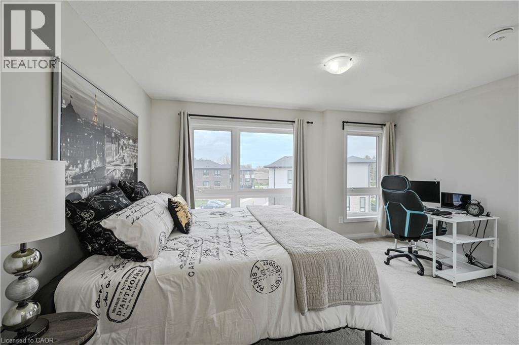 Carpeted bedroom featuring multiple windows with blinds, a ceiling-mounted light fixture, and neutral wall tones - 720 Grey Street Unit# 34, Brantford, ON - Indoor Photo Showing Bedroom