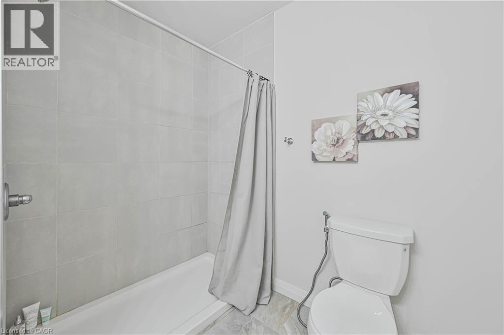 Bathroom featuring a white bathtub, light grey wall tiling, and a white toilet - 720 Grey Street Unit# 34, Brantford, ON - Indoor Photo Showing Bathroom