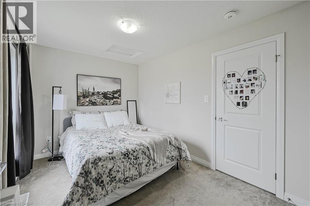 Carpeted room featuring a white paneled door, flush-mount ceiling light, and a window with dark curtains - 720 Grey Street Unit# 34, Brantford, ON - Indoor Photo Showing Bedroom