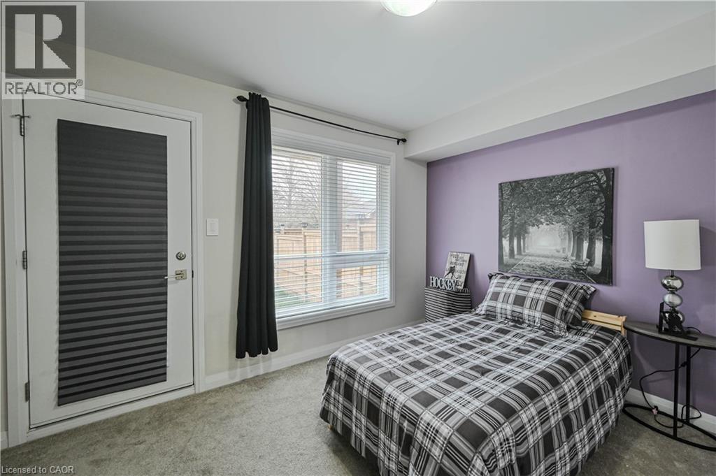 Carpeted room featuring a white door with integrated blinds, a window with horizontal blinds, and a light purple accent wall - 720 Grey Street Unit# 34, Brantford, ON - Indoor Photo Showing Bedroom