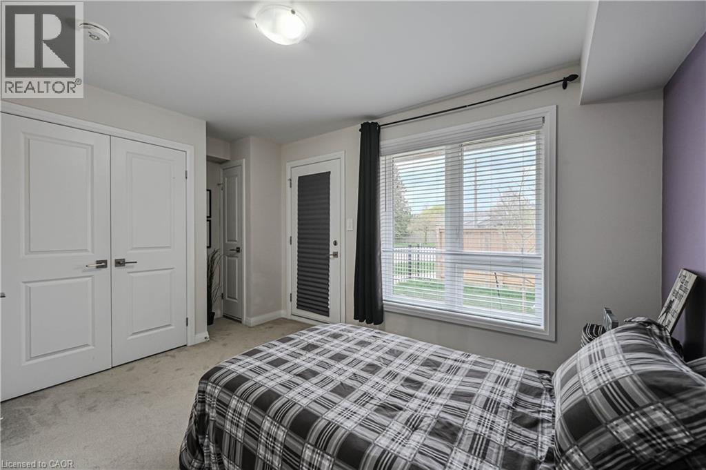 Bedroom featuring a large window with horizontal blinds, a white paneled door, a glass-paneled exterior door with internal blinds, and light gray wall-to-wall carpeting - 720 Grey Street Unit# 34, Brantford, ON - Indoor Photo Showing Bedroom