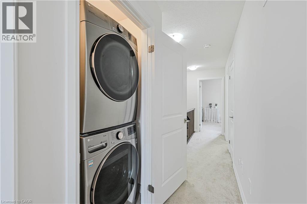 Hallway laundry closet featuring a stacked stainless steel washer and dryer - 720 Grey Street Unit# 34, Brantford, ON - Indoor Photo Showing Laundry Room