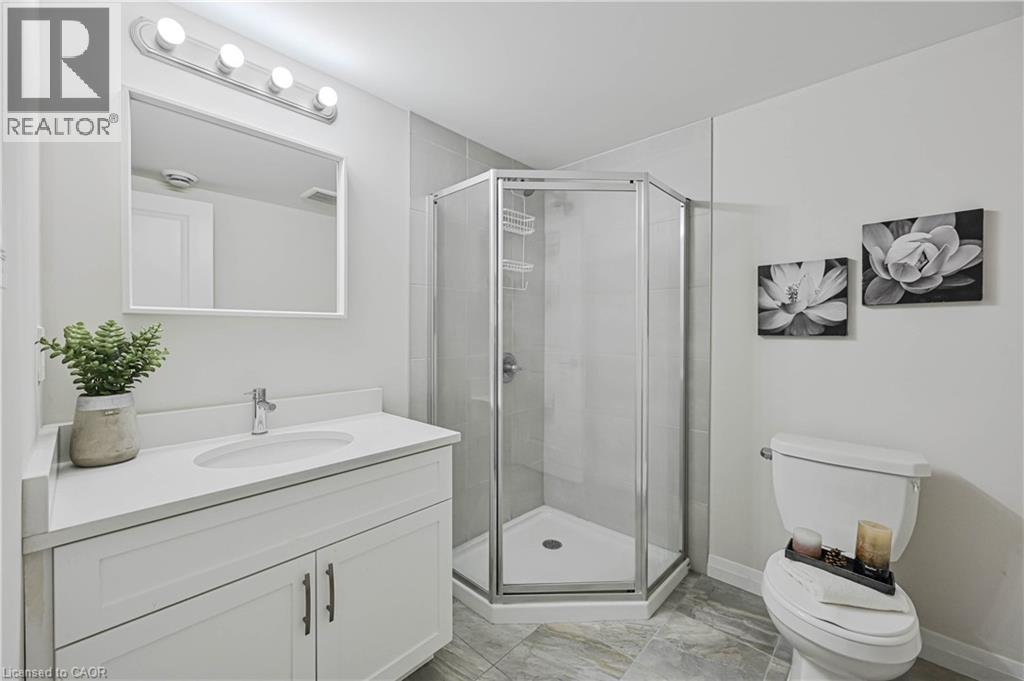 Modern bathroom featuring a white vanity with an integrated sink, a frameless rectangular mirror, and an enclosed corner shower with a glass door - 720 Grey Street Unit# 34, Brantford, ON - Indoor Photo Showing Bathroom