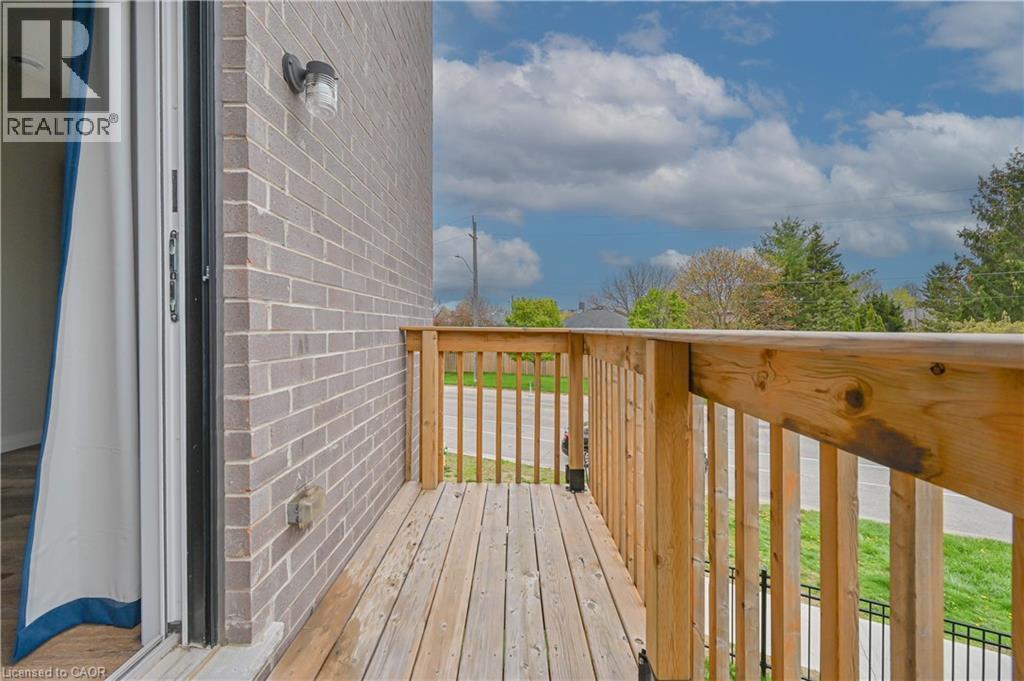 Private exterior balcony with wood decking and railing, gray brick exterior, and outdoor wall sconce - 720 Grey Street Unit# 34, Brantford, ON - Outdoor With Exterior
