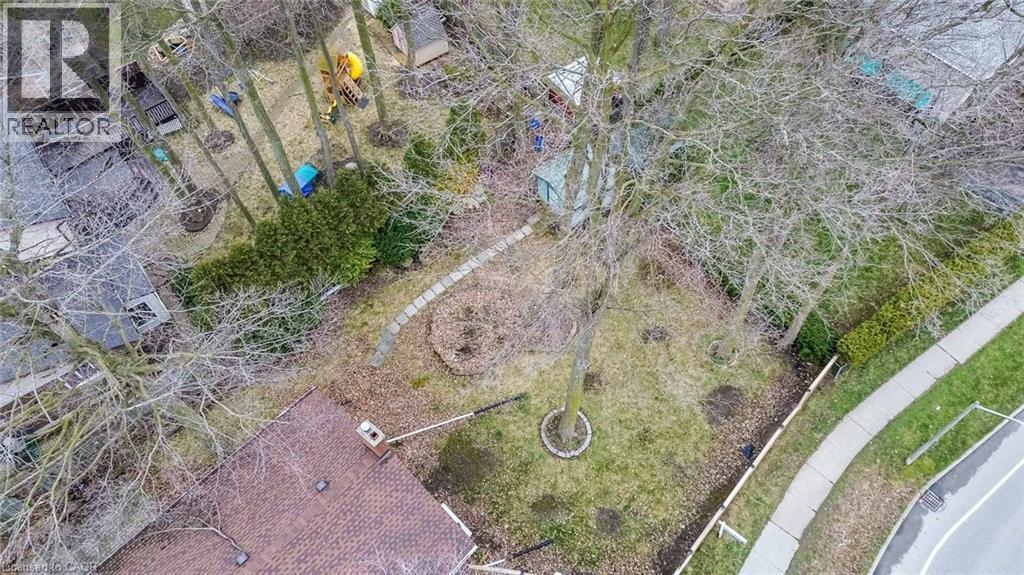 Spacious property featuring mature trees, a stone pathway, a side yard with landscaping, and a partial view of a shingled roofline - 462 Hazel Street, Waterloo, ON