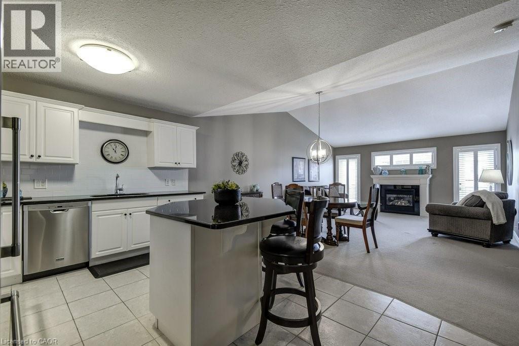 Open-concept living area featuring a kitchen with white cabinetry, stainless steel appliances, a black countertop island, and tile flooring - 605 Welland Avenue Unit# 21, St. Catharines, ON - Indoor Photo Showing Kitchen With Upgraded Kitchen