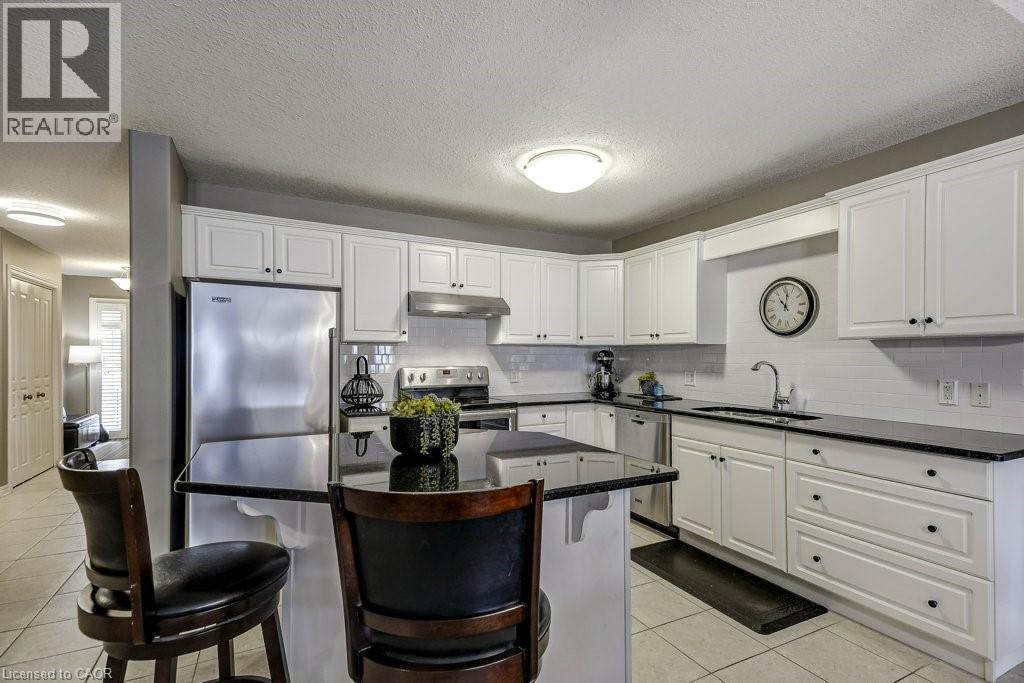 Bright kitchen featuring white cabinetry, dark countertops, stainless steel appliances, and a central island with bar seating - 605 Welland Avenue Unit# 21, St. Catharines, ON - Indoor Photo Showing Kitchen