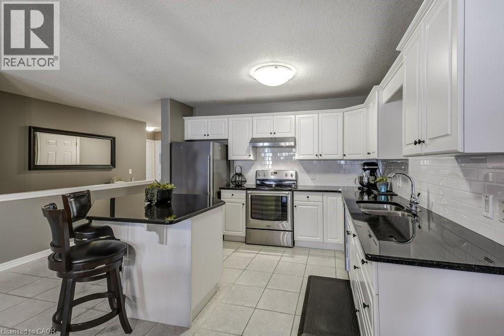 Contemporary kitchen featuring white cabinetry, dark countertops, stainless steel appliances, a subway tile backsplash, and light-toned floor tiles - 605 Welland Avenue Unit# 21, St. Catharines, ON - Indoor Photo Showing Kitchen With Double Sink