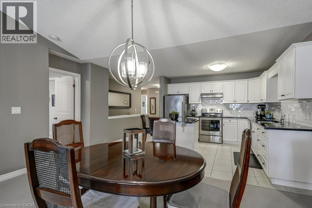 Open-concept dining area with a contemporary orb chandelier, wood-finish flooring, and direct sightlines to the kitchen featuring white cabinetry, stainless steel appliances, and a tiled backsplash - 605 Welland Avenue Unit# 21, St. Catharines, ON - Indoor