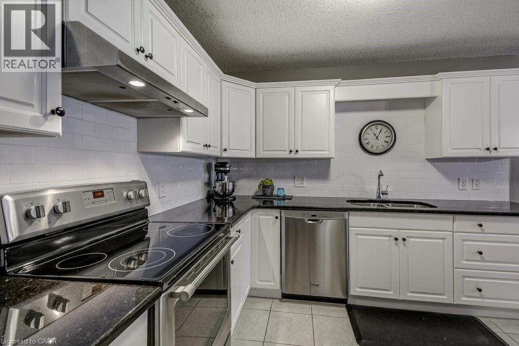 Kitchen featuring white cabinetry, dark countertops, tile flooring, a stainless steel range hood, and stainless steel appliances - 605 Welland Avenue Unit# 21, St. Catharines, ON - Indoor Photo Showing Kitchen With Double Sink