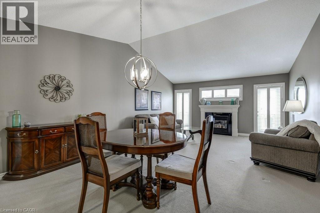 Spacious room featuring vaulted ceilings, a central spherical chandelier, a fireplace with a white mantel, and multiple windows with white blinds - 605 Welland Avenue Unit# 21, St. Catharines, ON - Indoor With Fireplace