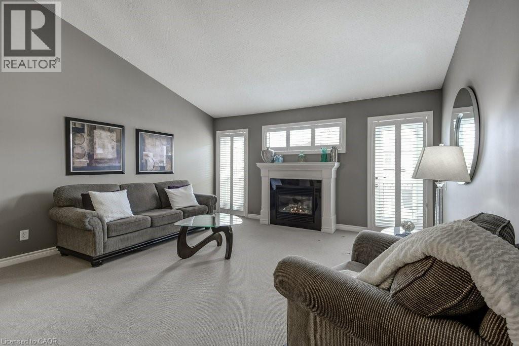 Living room featuring a gas fireplace with a white mantel, sloped ceiling, and light-colored carpeting - 605 Welland Avenue Unit# 21, St. Catharines, ON - Indoor Photo Showing Living Room With Fireplace