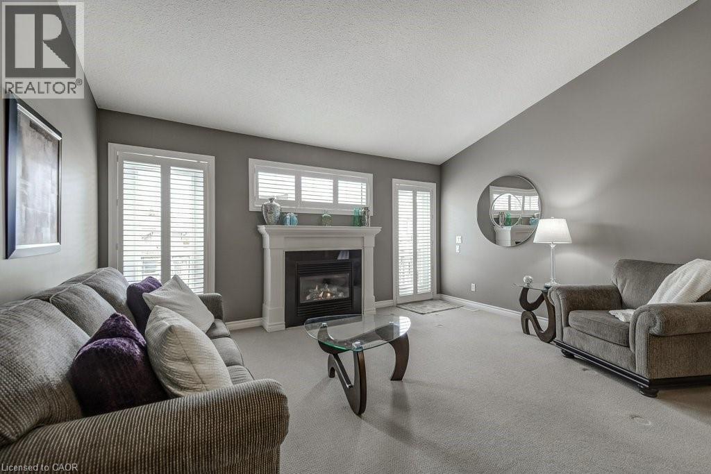 Living area featuring a gas fireplace with a white mantel, white plantation shutters, and light grey carpeting - 605 Welland Avenue Unit# 21, St. Catharines, ON - Indoor Photo Showing Living Room With Fireplace