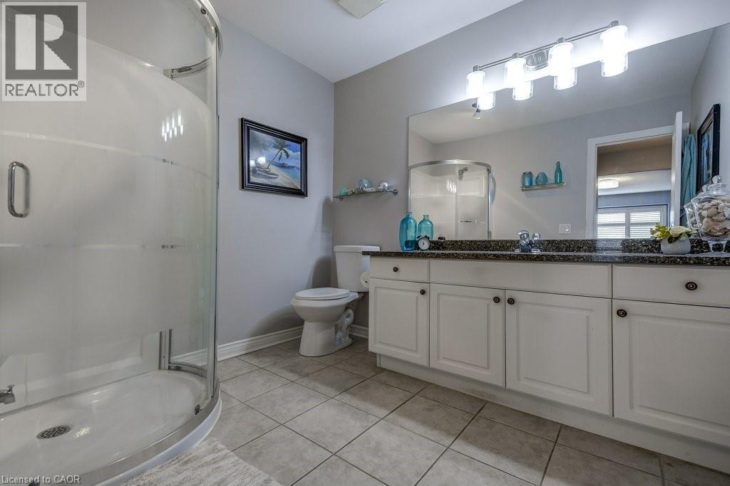 Bathroom featuring a curved glass shower enclosure, a white vanity with multiple cabinet doors, dark speckled countertop, and a large mirror with integrated lighting - 605 Welland Avenue Unit# 21, St. Catharines, ON - Indoor Photo Showing Bathroom