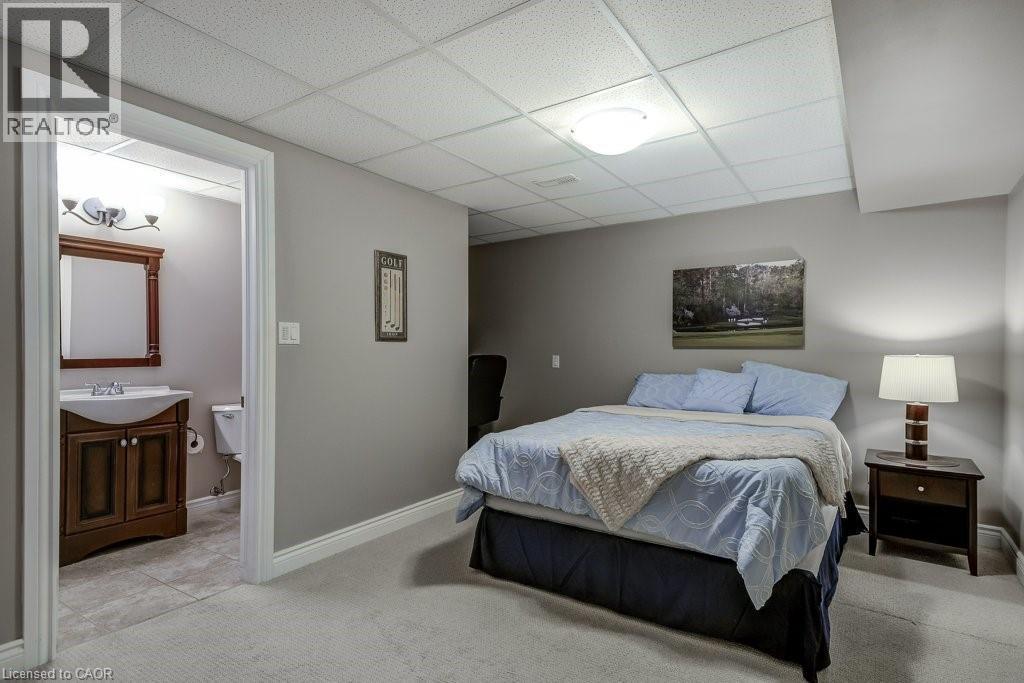 Carpeted room with drop ceiling and recessed lighting, offering direct access to a bathroom featuring a dark wood vanity with white sink, a framed mirror, and tile flooring - 605 Welland Avenue Unit# 21, St. Catharines, ON - Indoor Photo Showing Bedroom