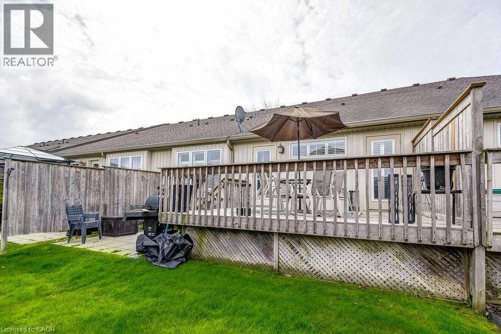 Rear property exterior featuring a raised wood deck, a ground-level patio, a fenced perimeter, and a green lawn - 605 Welland Avenue Unit# 21, St. Catharines, ON - Outdoor With Deck Patio Veranda