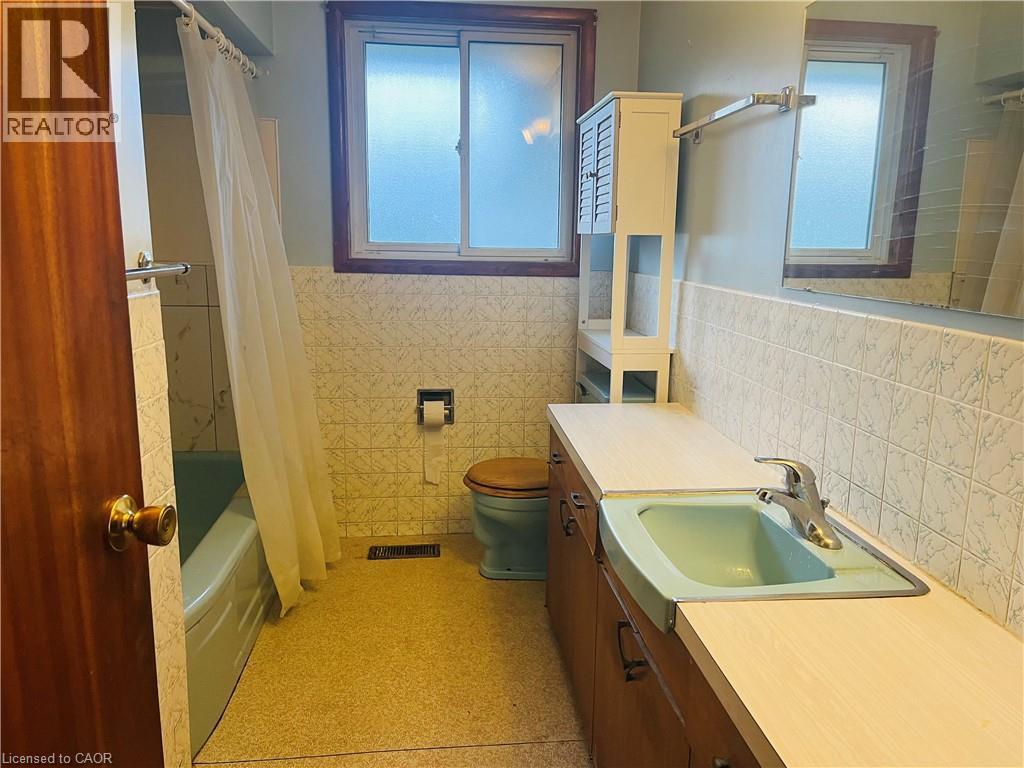 Bathroom featuring a basin sink with chrome faucet, wood-finish vanity, tiled walls, and a window with wood trim - 157 Schweitzer Street, Kitchener, ON - Indoor Photo Showing Bathroom