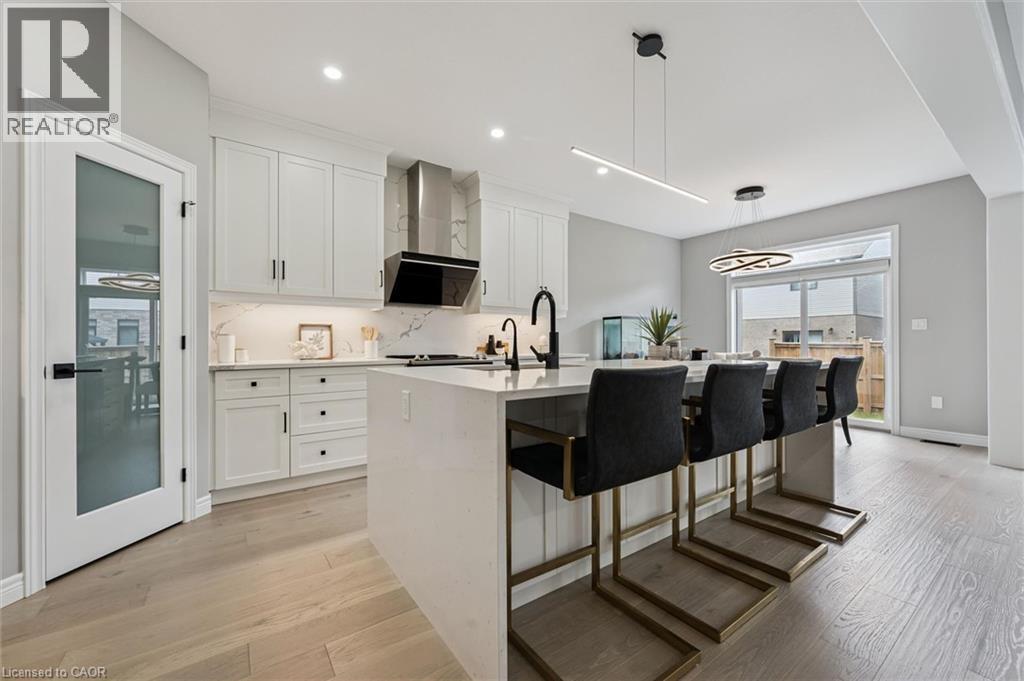 Contemporary kitchen featuring a waterfall island with seating, white shaker cabinetry, and wood-finish flooring - 628 Florencedale Crescent, Kitchener, ON