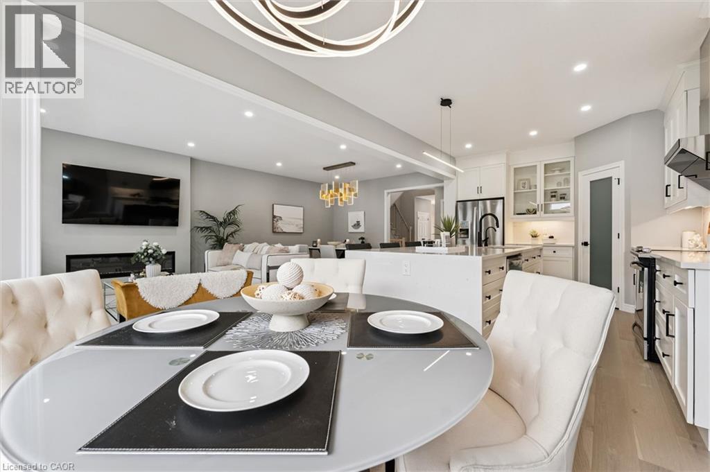 Open-concept living space featuring a contemporary dining area with a round glass-top table, light wood-finish flooring, a modern linear chandelier, and recessed lighting throughout - 628 Florencedale Crescent, Kitchener, ON