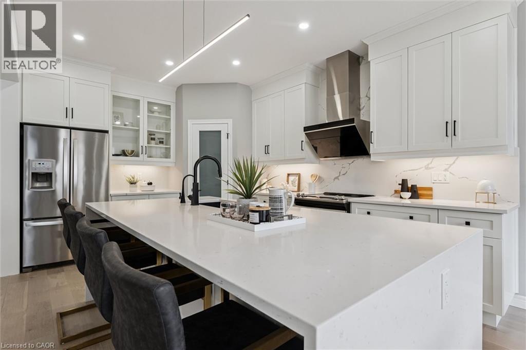 Modern kitchen featuring a large white island with seating, stainless steel appliances, white cabinetry with black hardware, and a matching white countertop and backsplash - 628 Florencedale Crescent, Kitchener, ON