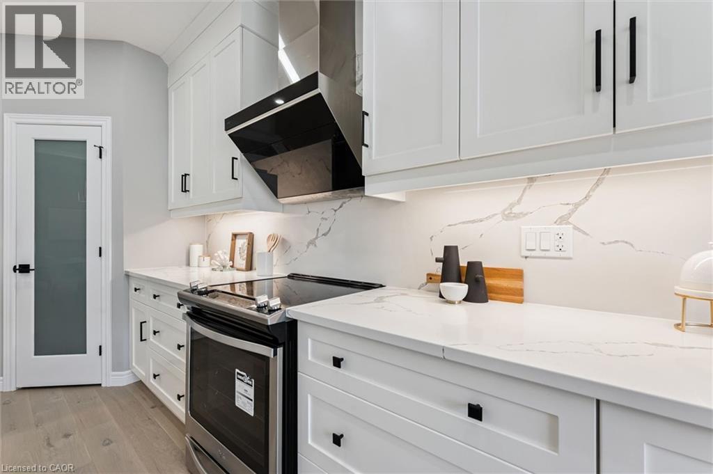 Contemporary kitchen featuring white shaker cabinetry, stainless steel range with overhead ventilation, light-toned countertops with integrated backsplash, and wood-finish flooring - 628 Florencedale Crescent, Kitchener, ON