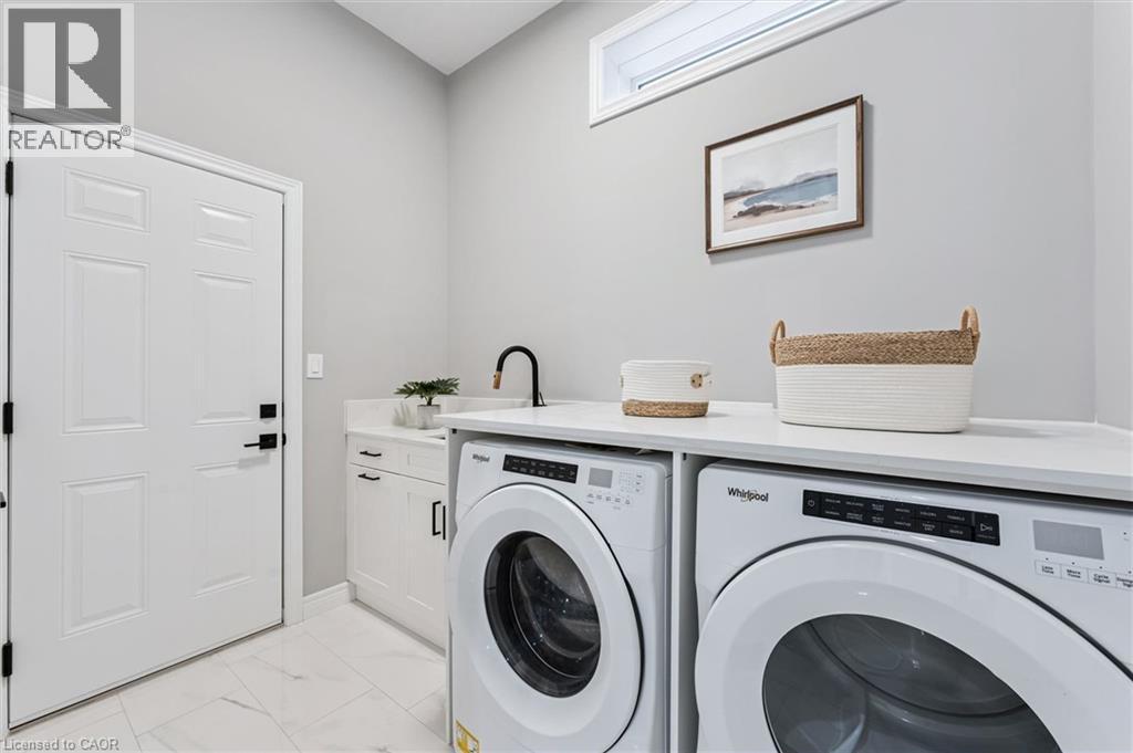 Dedicated laundry space featuring white cabinetry, a built-in sink with a matte black faucet, and a light-colored countertop spanning across the appliances - 628 Florencedale Crescent, Kitchener, ON