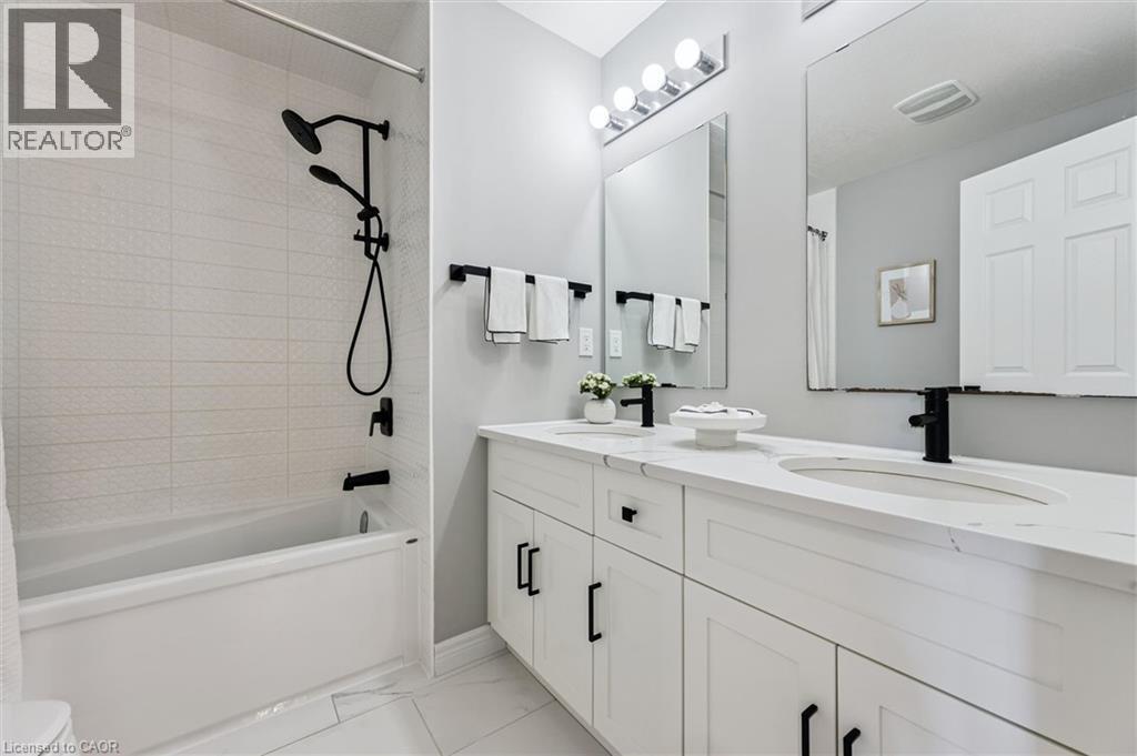Bathroom featuring a white subway tile tub surround with matte black fixtures, a white bathtub, and a dual vanity with white cabinetry, integrated sinks, and matte black faucets - 628 Florencedale Crescent, Kitchener, ON