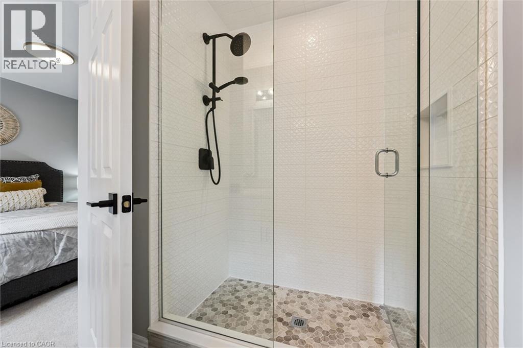 Glass-enclosed shower with a matte black shower system, textured white subway tile, a recessed shower niche, and hexagonal floor tiling - 628 Florencedale Crescent, Kitchener, ON