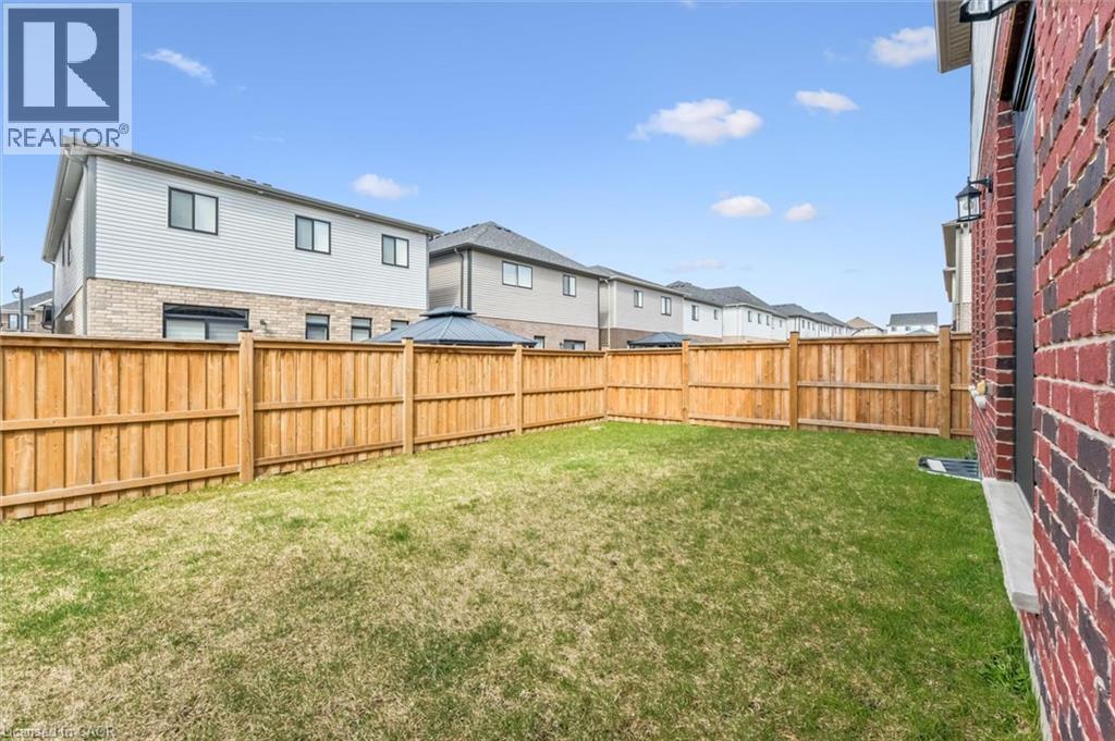 Spacious backyard featuring a manicured lawn, full perimeter wood fencing, and a red brick exterior wall - 628 Florencedale Crescent, Kitchener, ON