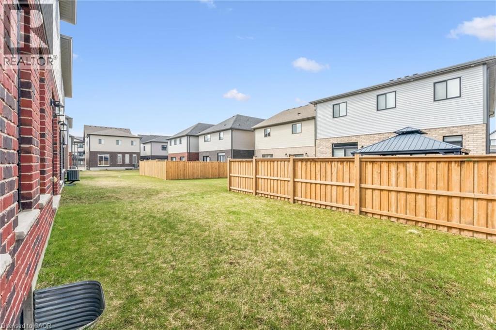 Expansive backyard featuring a manicured lawn, a full-height wood privacy fence, and a red brick exterior wall with a foundation window well - 628 Florencedale Crescent, Kitchener, ON