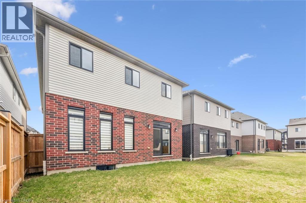 Red brick and light-colored siding exterior, featuring multiple windows with dark frames, a ground-level sliding glass door, and a wooden fence bordering the property - 628 Florencedale Crescent, Kitchener, ON
