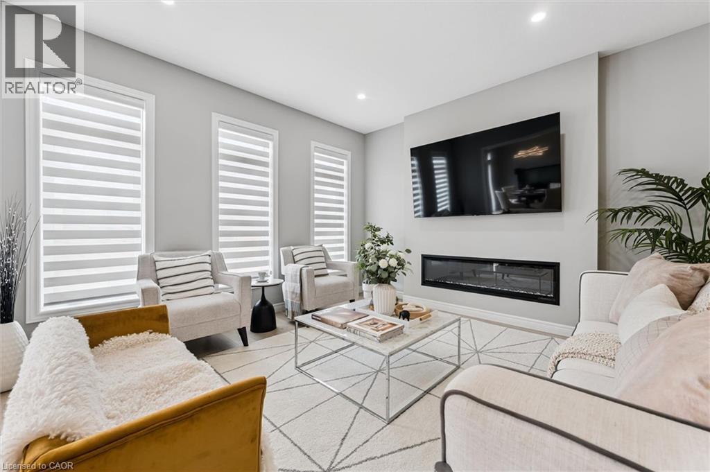 Living room featuring a built-in linear fireplace, wall-mounted television, recessed lighting, three vertical windows with modern blinds, and light-toned wall finishes - 628 Florencedale Crescent, Kitchener, ON