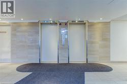 Building lobby featuring two elevator doors with brushed metal frames, recessed lighting, tile flooring, and textured wall accents - 