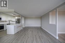 Open-concept kitchen and living area featuring wood-finish flooring, white cabinetry, stainless steel appliances, a white tile backsplash, and a kitchen island with seating - 
