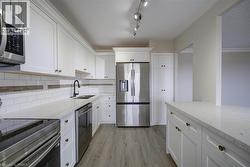 Modern kitchen featuring white shaker cabinetry with gold-toned hardware, light-toned countertops, stainless steel appliances, and wood-finish flooring - 