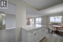 Open-concept living area featuring light wood-finish flooring, a white kitchen island with a light-toned countertop and cabinet storage, and a dining area with a chandelier - 