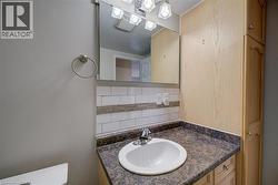 Bathroom featuring a single basin vanity with a patterned countertop, subway tile backsplash with decorative accent, and a wood-finish storage cabinet - 