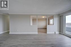 Spacious living area featuring light wood-finish flooring, neutral wall paint, white baseboards, and crown molding - 