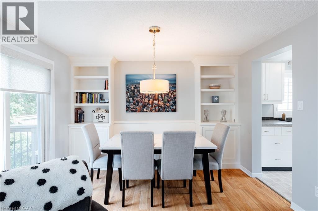 Dining area featuring wood-finish flooring, built-in shelving, a drum pendant light fixture, and a window with roller shade - 560 Penny Lane, Waterloo, ON